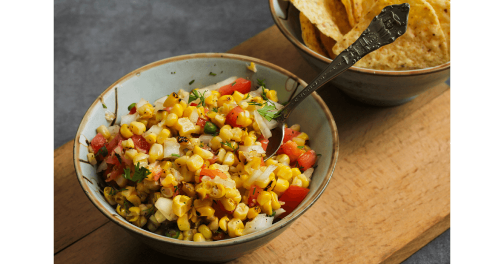 Grilled corn salsa in a bowl accompanied by a side of tortilla chips, featuring vibrant colors and a fresh, homemade appearance, perfect for a summer snack or appetizer.