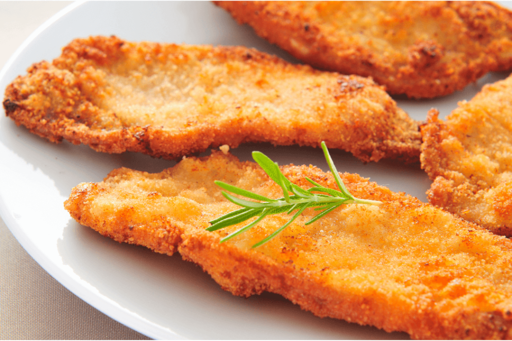 Chicken Milanese: Breaded chicken cutlet served with a side of arugula salad and lemon wedges.

