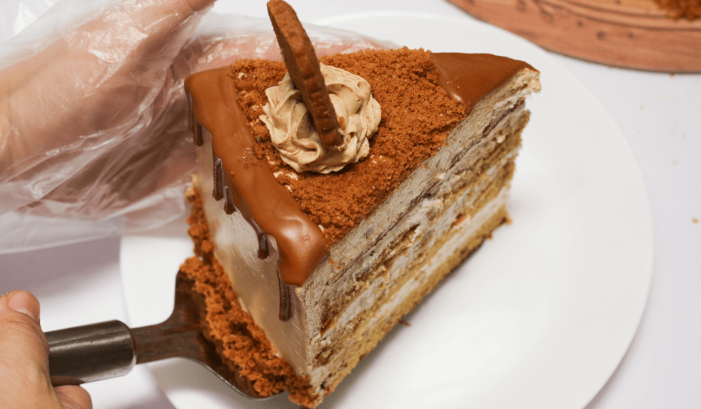 A person delicately cuts a slice of Biscoff Cheesecake on a plate, ready to indulge in its creamy and irresistible goodness.